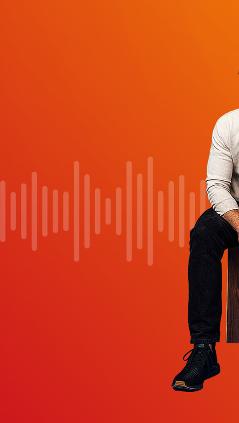 A man sits on a wooden stool in front of a red-to-orange gradient background with stylized sound waves stretching horizontally across the image. A man sits on a wooden stool in front of a red-to-orange gradient background with stylized sound waves stretching horizontally across the image.