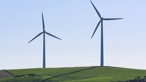 Two wind turbines on a green field, in the background light blue sky Two wind turbines on a green field, in the background light blue sky