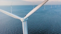 Close-up of the rotor of a wind turbine taken from bird perspective, with more wind turbines in the backdrop, standing in a row in a sea with waves.  Close-up of the rotor of a wind turbine taken from bird perspective, with more wind turbines in the backdrop, standing in a row in a sea with waves.