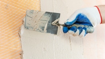 A worker is applying plaster to the mash on the wall with a trowel. A worker is applying plaster to the mash on the wall with a trowel.