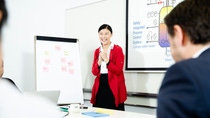 A BASF employee stands in front of a flipchart and presentation screen, smiling while leading a meeting, with colleagues listening in the foreground. A BASF employee stands in front of a flipchart and presentation screen, smiling while leading a meeting, with colleagues listening in the foreground.