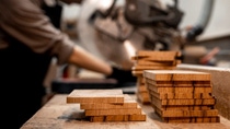 Wooden boards lying on a table. In the background a man is working with the wooden boards. Wooden boards lying on a table. In the background a man is working with the wooden boards.