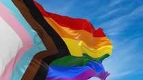 Waving rainbow flag with blue sky in the background.