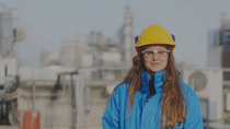 An engineer wearing a hard hat and safety goggles stands in front of an industrial plant. An engineer wearing a hard hat and safety goggles stands in front of an industrial plant.