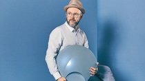 Profile shot of Mark Gutjahr holding a large gray-blue bowl in his hands and sitting on a box. Profile shot of Mark Gutjahr holding a large gray-blue bowl in his hands and sitting on a box.