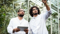 Male scientist pointing while colleague holding digital tablet against greenhouse Male scientist pointing while colleague holding digital tablet against greenhouse