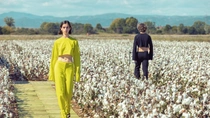 Un défilé de mode a lieu dans un champ de coton, avec des mannequins entre les cotonniers. Une femme portant une tenue jaune vif se dirige vers l’appareil photo. Un défilé de mode a lieu dans un champ de coton, avec des mannequins entre les cotonniers. Une femme portant une tenue jaune vif se dirige vers l’appareil photo.