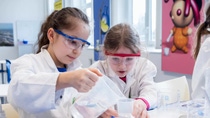 Two young girls in goggles and white lab coats experiment with water. Two young girls in goggles and white lab coats experiment with water.