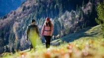 Un homme et une femme traversent une prairie de montagne par une journée ensoleillée. Ils portent des vêtements chauds d’extérieur. Un homme et une femme traversent une prairie de montagne par une journée ensoleillée. Ils portent des vêtements chauds d’extérieur.