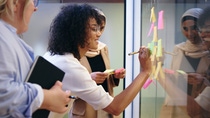 Female office employee writes down on Post its on a glass wall Female office employee writes down on Post its on a glass wall