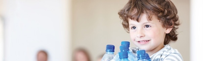 Cute boy holding empty water bottles with his parents in the background