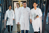 A group of scientists in lab coats walk through a modern corridor. A group of scientists in lab coats walk through a modern corridor.