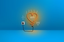 The picture shows an orange neon light in the form of a heart plugged into a blue wall. There are white sketches around it of a wind turbine, an electric heating element and the number “850°C”. The picture shows an orange neon light in the form of a heart plugged into a blue wall. There are white sketches around it of a wind turbine, an electric heating element and the number “850°C”.