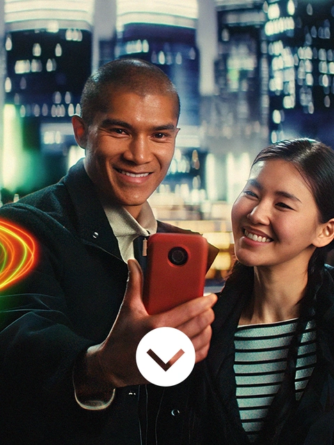 Un homme et une femme portant des vestes décontractées se tiennent devant une ligne d’horizon urbaine en Asie, la nuit. Ils regardent tous les deux le téléphone tenu par l’homme. Des tourbillons lumineux apparaissent à côté d’eux. Un homme et une femme portant des vestes décontractées se tiennent devant une ligne d’horizon urbaine en Asie, la nuit. Ils regardent tous les deux le téléphone tenu par l’homme. Des tourbillons lumineux apparaissent à côté d’eux.