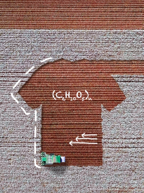 The picture is an aerial view of a cotton field, where a harvesting machine is working. The soil showing where the cotton has been harvested is in the shape of a T-shirt. There are white handwritten sketches on the picture showing scientific formulae and three arrows. 