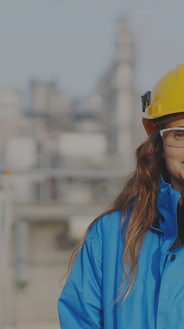 An engineer wearing a hard hat and safety goggles stands in front of an industrial plant. An engineer wearing a hard hat and safety goggles stands in front of an industrial plant.