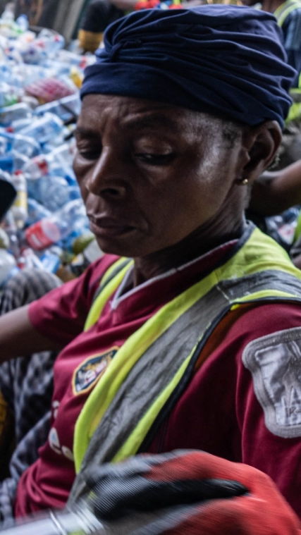 Three people sorting through a large pile of plastic bottles. 