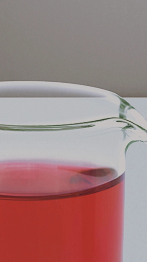 Many glass containers and test tubes with coloured liquids stand in front of a monitor on which scientific formulas can be seen.