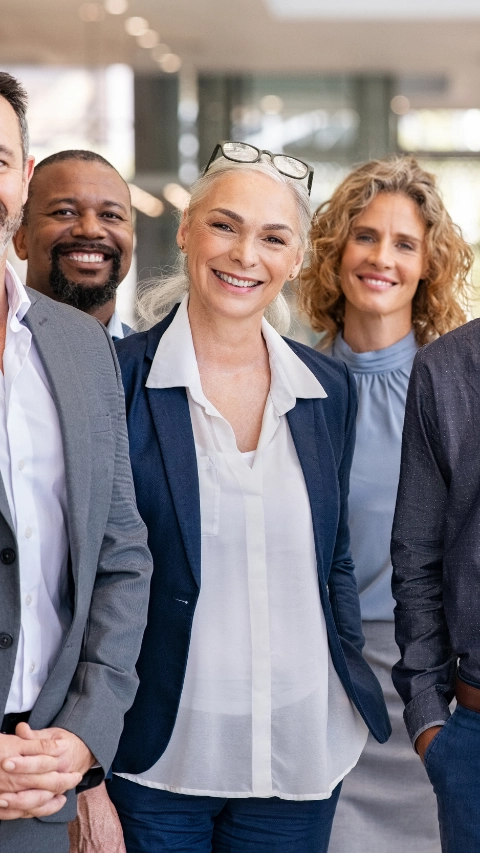 Portrait of successful group of business people at modern office looking at camera. Portrait of happy businessmen and satisfied businesswomen standing as a team. Multiethnic group of people smiling and looking at camera.