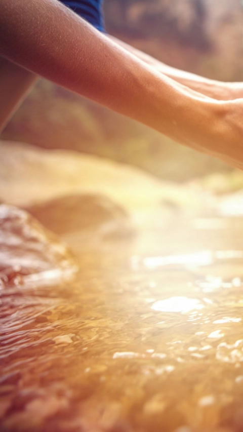 Human hand cupped to catch the fresh water from the river, reflection on water surface.