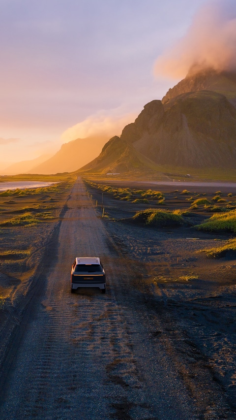 Gravel road at a golden Sunset with Vestrahorn mountain in the background and a car driving the road in Iceland