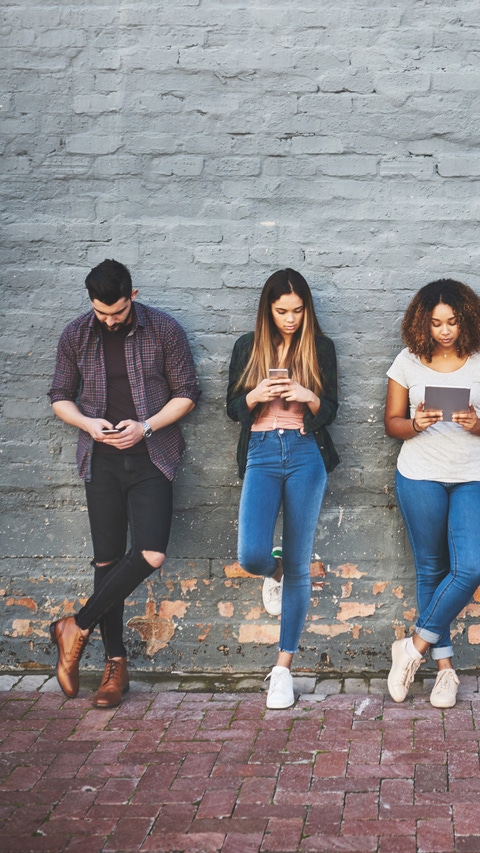 Shot of a group of young people using their wireless devices together outdoors