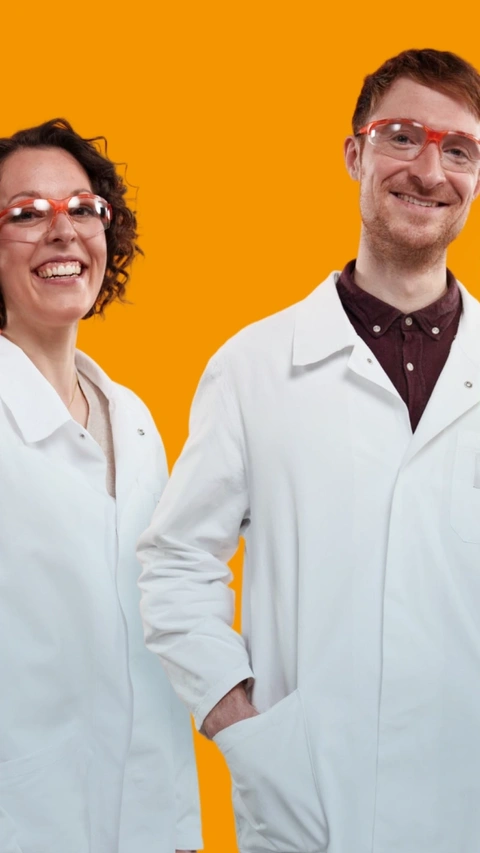 Deux scientifiques BASF portant des blouses de laboratoire blanches et des lunettes de sécurité se tiennent devant un fond orange, souriant. Un tourbillon lumineux flotte à côté d’eux. Deux scientifiques BASF portant des blouses de laboratoire blanches et des lunettes de sécurité se tiennent devant un fond orange, souriant. Un tourbillon lumineux flotte à côté d’eux.