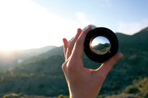 A hand is holding a lens in front of a mountain, focusing on the summit A hand is holding a lens in front of a mountain, focusing on the summit